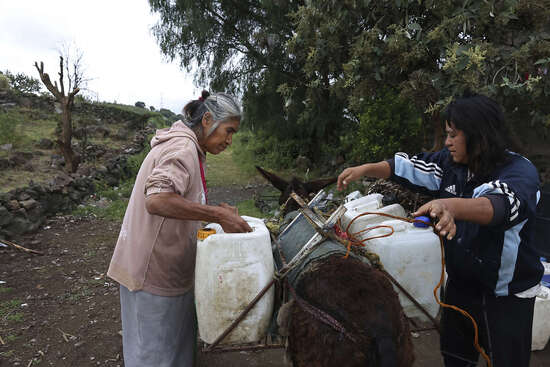 Emilia Segura, left, and her daughter Cecilia Rivera Segura arrange containers after filling them with water at a free, public well in Pueblo Santa Cruz Acalpixca, Xochimilco, on the outskirts of Mexico City, Saturday, Oct. 7, 2023. Segura, 62, has been selling water daily for over a decade with the help of her four donkeys. The system which provides the capital with over a quarter of its drinking water is 44% lower than it should be and have set a new record, according to government figures, and authorities have begun cutting water to the city.