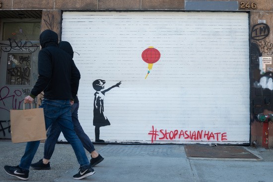 NEW YORK, NEW YORK - MARCH 19: People wearing masks walk past street art that looks like Banksy's "Tribute Girl with Balloon" but with a red Chinese lantern and reads, "Stop Asian Hate" by Adrian Wilson on March 19, 2021 in New York City. After undergoing various shutdown orders for the past 12 months the city is currently in phase 4 of its reopening plan, allowing for the reopening of low-risk outdoor activities, movie and television productions, indoor dining as well as the opening of movie theaters, all with capacity restrictions. (Photo by Alexi Rosenfeld/Getty Images)