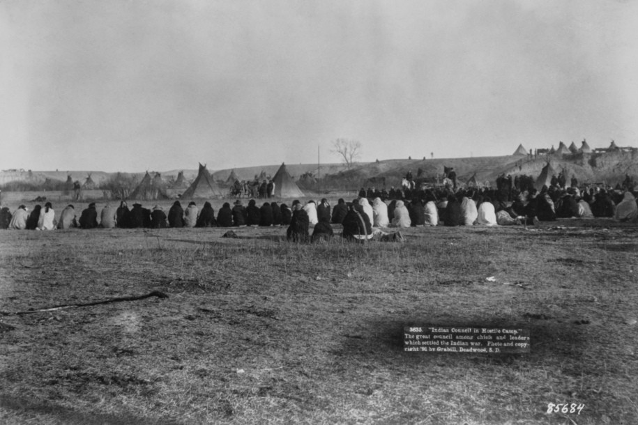 Native American Lakota men sitting on the ground, with teepees in the background, during peace negotiations between Lakota leaders and United States Army Officer in the northern badlands of Pine Ridge Indian Reservation, South Dakota, January 1891. The negotiations are being held following the Wounded Knee Massacre. (Photo by John C. H. Grabill/FPG/Archive Photos/Getty Images)