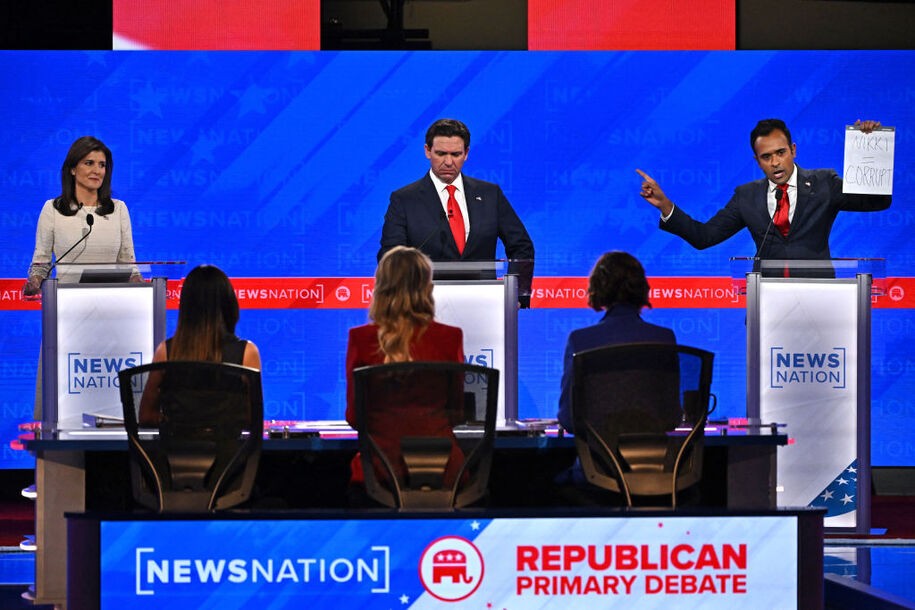 TOPSHOT - Entrepreneur Vivek Ramaswamy (R) holds up a sign reading 'Nikki = corrupt' referring to former Governor from South Carolina and UN ambassador Nikki Haley (L), as Florida Governor Ron DeSantis (C) looks on, during the fourth Republican presidential primary debate at the University of Alabama in Tuscaloosa, Alabama, on December 6, 2023. (Photo by Jim WATSON / AFP) (Photo by JIM WATSON/AFP via Getty Images)